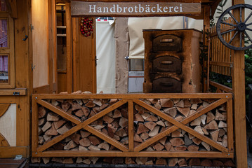 Old ovens with firewood stacks and nameplate with inscription "Bakery" in German language. Rustic wooden decorations at Christmas fair in Berlin Germany. Log cabin with traditional stone oven.