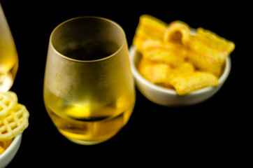 glass of whiskey with ice cubes and salty snacks on the background of the bar