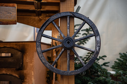 Weathered wood cart wheel and conifer tree branches on background. Farm wagon carriage wheel closeup. Aged wooden texture. Rustic wooden decorations at Christmas fair in Berlin Germany.