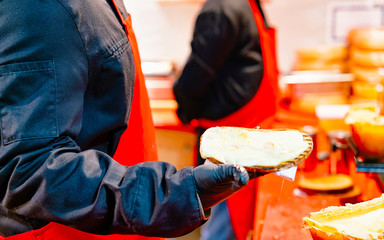 Raclette Melting Cheese Food in Night Christmas Market at Gendarmenmarkt in Winter Berlin, Germany. Advent Fair and Stalls with Food on the Bazaar.