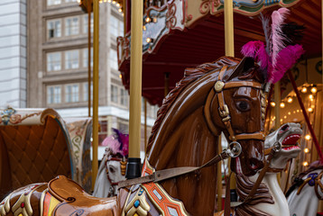 Fototapeta na wymiar Carousel in park. Closeup of horse head of brown toy horse with purple and pink plumage. Vintage traditional carousel. Retro colorful illuminated merry-go-round. Funfair at Christmas market in Europe