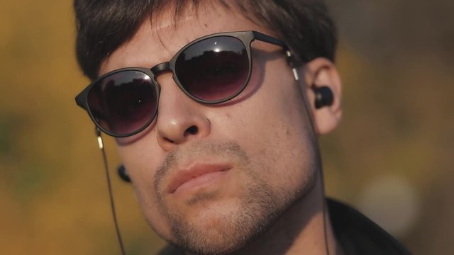 Close-up of a man's face with blurred background in sunglasses with wireless headphones