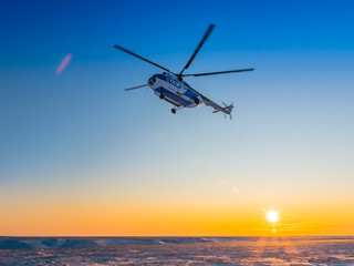Arctic winter day in the Arctic. The low sun. The sun's rays illuminate the snow on the tundra. In the clear sky a helicopter in the backlight.