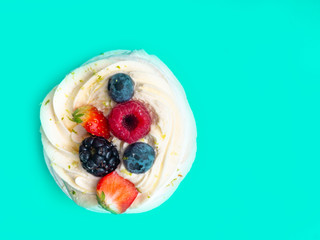 Meringue cake Pavlova with fresh ripe raspberry, strawberry, blueberry, whipped cream on trendy green mint color background, festive confetti