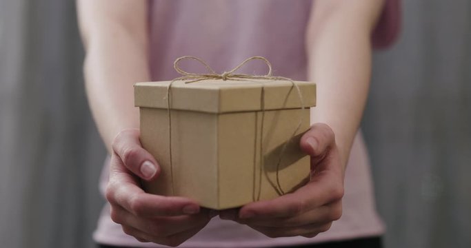 Slow motion young woman stand and show brown gift box with twine bow