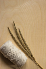 Three ears on a wooden background next to a skein of thread of natural color. Three ears of wheat lie on a yellow-veined wooden surface and a coil of twine