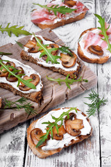 Bruschetta with cream cheese, roasted champignons and arugula against the white wooden background
