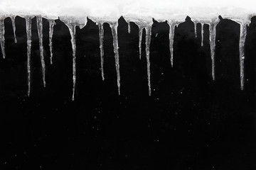 Obraz na płótnie Canvas Winter or spring background concept. Row of icicles on wet black textured wall, with falling snow. Copy space.