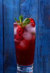 Red beverage with ice cubes, raspberries, strawberries and mint against the blue wooden background