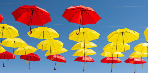 Fototapeta na wymiar Colourful umbrellas urban street decoration. Hanging colorful umbrellas over blue sky, tourist attraction