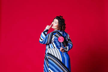 Plus size model in blue dress with big lollipop, fat woman on red background