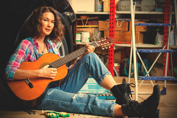 Fototapeta na wymiar beautiful Woman mechanic in blue overalls resting with a guitar