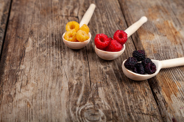 Ripe red and yellow raspberries and blackberries in spoons