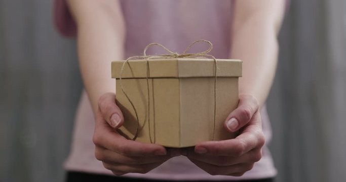 Slow motion young woman stand and show brown gift box with twine bow
