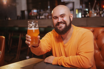 Happy handsome bearded man smiling cheerfully toasting with his beer glass at the pub