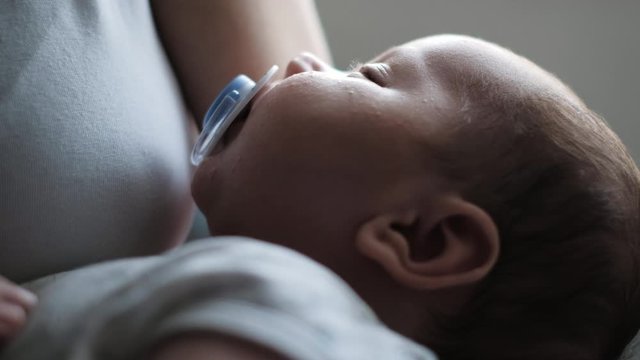 Close Up of Newborn baby sleeping over the mother chest and sucks a pacifier