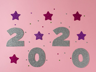 Celebrating the new year 2020. Silver mother-of-pearl paper, number 2020 with pink stars and...