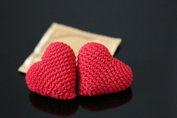 Two red knitted hearts and condom on dark glass table. Concept of contraception, safety sex