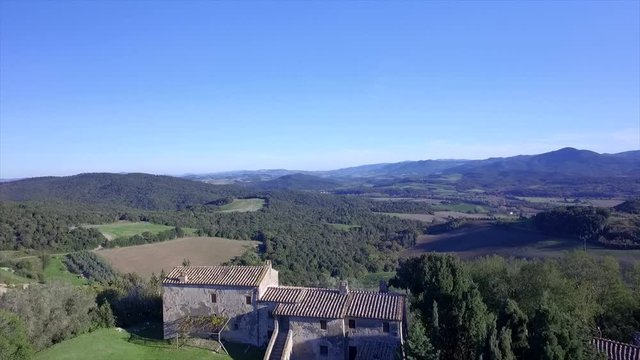 4k aerial  drone backward flight footage at midday time over the Tuscany countryside hills and the small ancien village of Gello near Volterra.