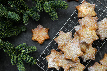 Cookies with almonds on a stand, with icing sugar, with Christmas tree branches on a dark relief background.