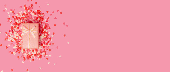 pink gift box with a bow in the center of the frame on a background of scattered little sweet candy hearts on a pink background. view from above