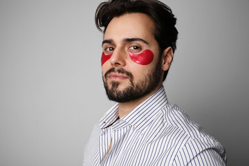 Portrait of young bearded man using hydrating red patches. Space for text.