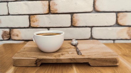Americano coffee in a white ceramic cup placed on a wooden tray, the background is white brick