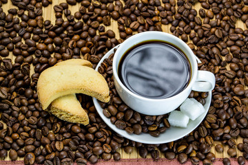 a cup of coffee with cookies, coffee grains scattered on a table near a cup with a coffee, selective focus