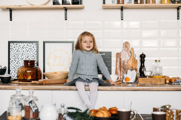 Smiling girl is sitting on kitchen table. Little girl in kitchen at home. Christmas morning