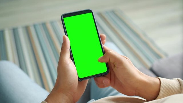 Male palms holding smartphone with mock-up green screen touching with fingers surfing internet enjoying online content. People and electronics concept.