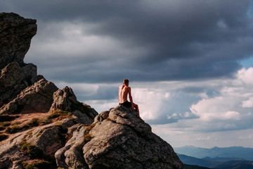 A guy sits on a stone in the mountains and looks into the distance. Rest after a difficult climb