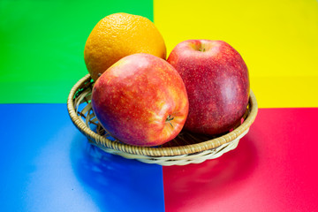 fresh apples in a straw basket with orange on a colored background