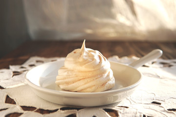    Homemade white meringue cake on cosy plate and rustic napkin, wooden table near window. French or Italian dessert made of eggs and sugar. Selective focus.         
