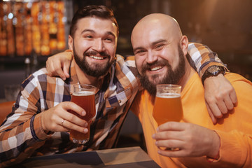 Two cheerful male friends embracing, drinking beer together at the pub