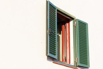 Window with open shutters and sashes on a light plastered wall.