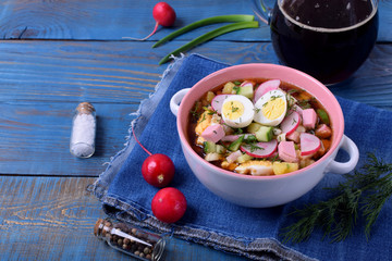 Russian cold soup Okroshka with vegetables, sausage, eggs and kvass in a ceramic bowl on the blue table