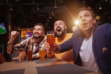 Low angle shot of three excited men screaming happily, celebrating victory of their favourite football team. Soccer fans drinking at beer pub, watching a game © mad_production