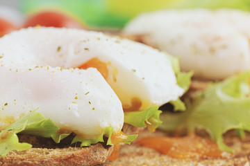 Poached egg with a notch close-up, lettuce and tomatoes on the background.