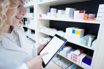 Pharmacist holding tablet by the shelf full of medicine in drug store and checking medication availability and specification. Pharmacy and health care.