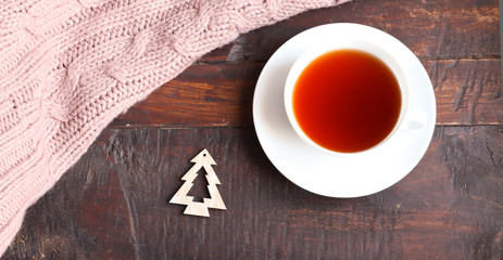A cup of tea, a small christmas tree decoration and pink knitted texture on an old wooden background. 