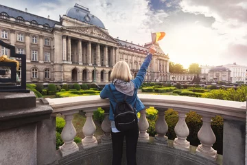 Foto op Aluminium A female tourist stands with the flag of Belgium against the backdrop of the Royal Palace in Brussels. © LALSSTOCK