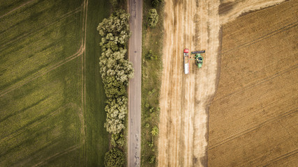 Aerial view of a combine unloads grain from grain compartment into a truck. One truck drove off and the next truck drove up to receive wheat grains.