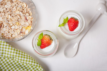 Two portions natural homemade yogurt in a glass jar with fresh strawberry and muesli nearby