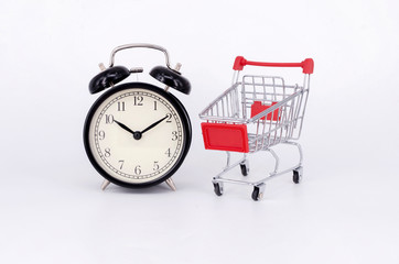 Shopping cart and classic alarm clock on white background. Sale time buy mall market shop consumer concept. Selective focus.