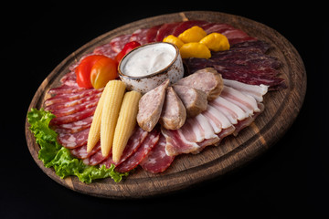 Appetizer with different sausages and pickled vegetables on wooden board isolated on a black.