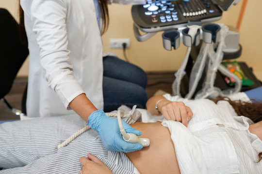 doctor moving ultrasound transducer on a woman's belly while looking at screen in hospital