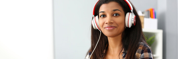 Black smiling woman sitting at workplace wearing headphones