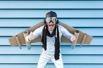man in silver suit with glasses and aviator helmet and cardboard plane wings - obrazy, fototapety, plakaty