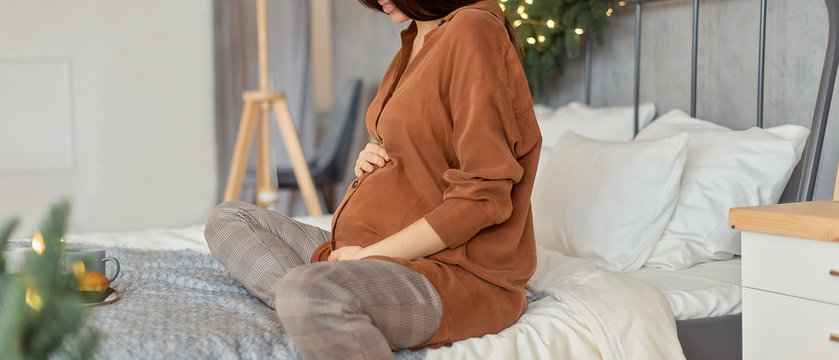 Pergnant womani on bed in christmas decorated room at Christmas morning