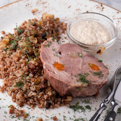 Boiled pork with buckwheat cereal served with fork and knife. Closeup